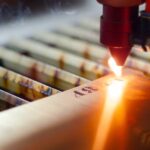 A laser engraving machine in a manufacturing facility is marking numbers into metal plating. A spark is visible.