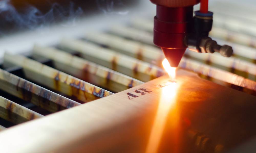 A laser engraving machine in a manufacturing facility is marking numbers into metal plating. A spark is visible.