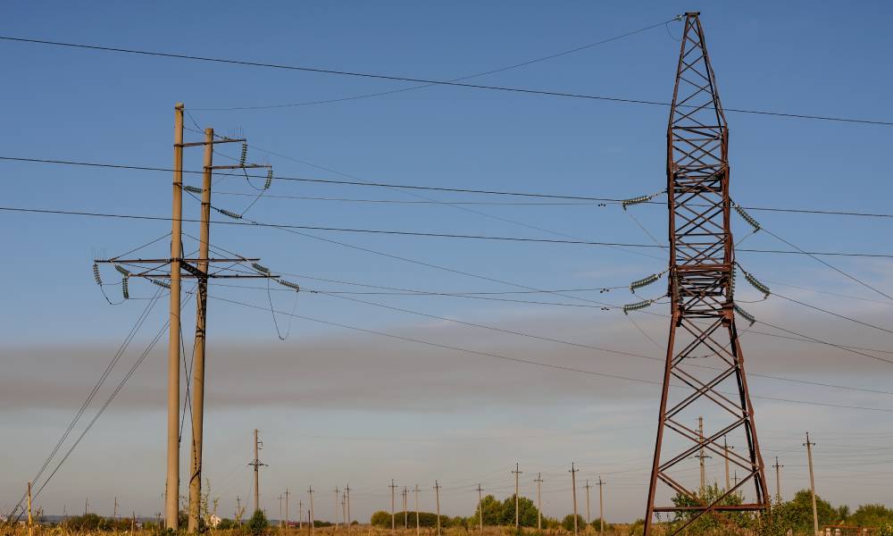 Two large utility towers standing in a field with a blue sky behind them and several smaller utility poles in the distance.