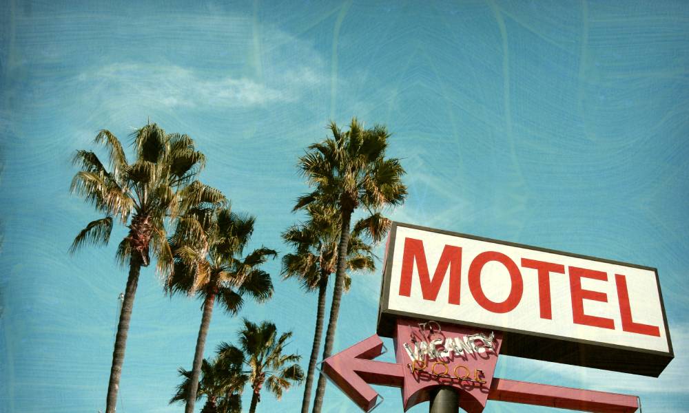A retro and aged roadside motel sign overlooking palm trees and blue skies, invoking Americana spirit.
