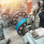 A team of maintenance technicians service a large mechanical power generation motor with wrenches and other repair tools.