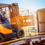An all-terrain forklift and trained driver loading materials on and off a semi-truck by using the safety ramp.