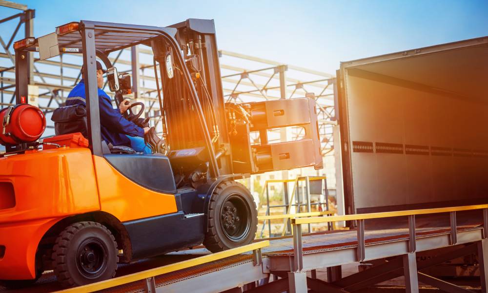 An all-terrain forklift and trained driver loading materials on and off a semi-truck by using the safety ramp.