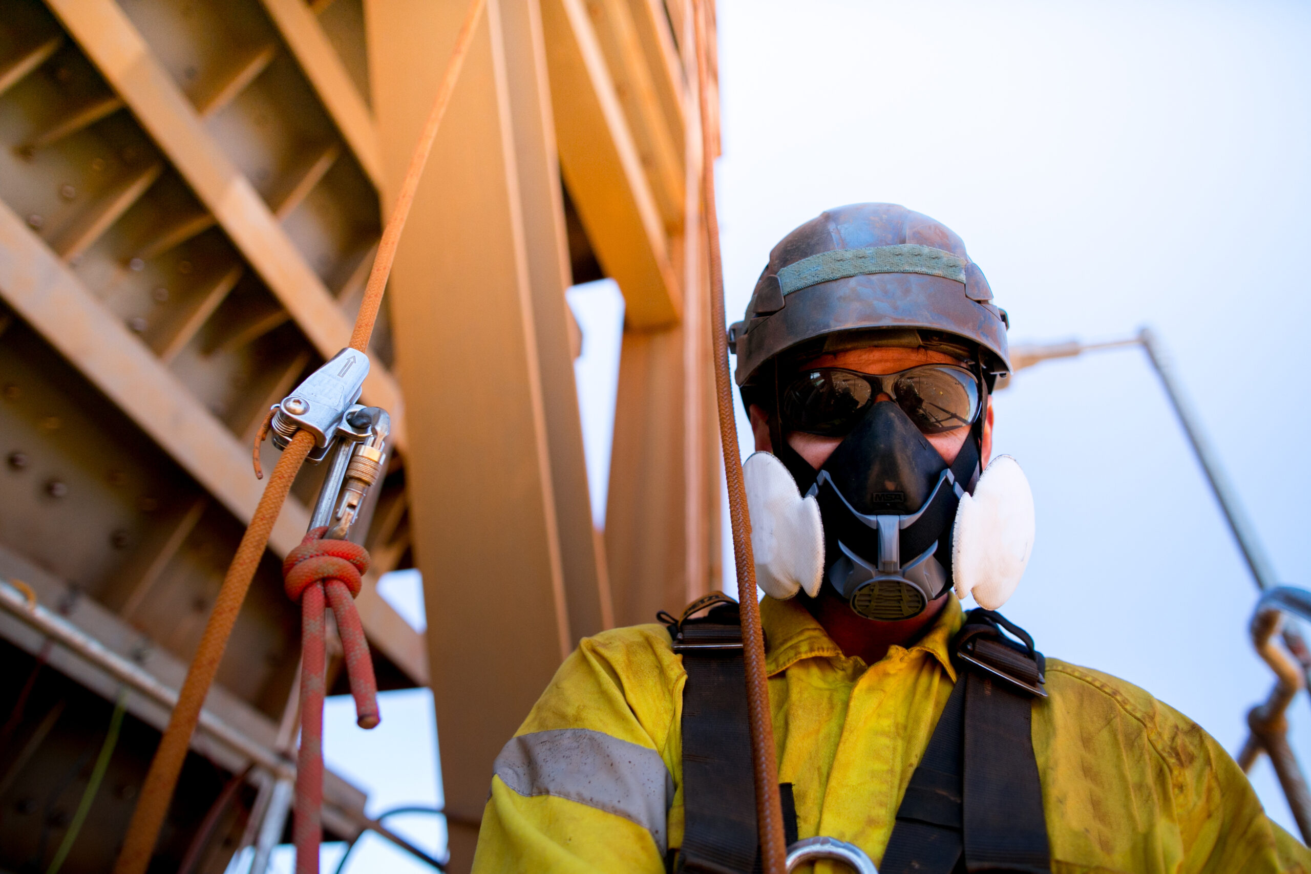 Male industrial rope access welder wearing P3 mask, mandatory protection harness, and helmet safety equipment.