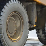 Three large tires sit on the wheels underneath a dump truck. The tires are wet and have mud on them.