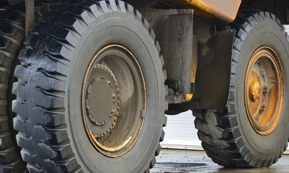 Three large tires sit on the wheels underneath a dump truck. The tires are wet and have mud on them.