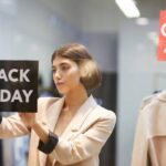 A woman in a suit sticking a black sign that reads "Black Friday" on it to the inside of a store's display window.