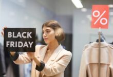 A woman in a suit sticking a black sign that reads "Black Friday" on it to the inside of a store's display window.