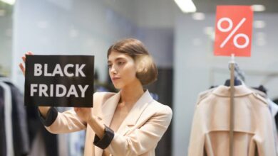 A woman in a suit sticking a black sign that reads "Black Friday" on it to the inside of a store's display window.