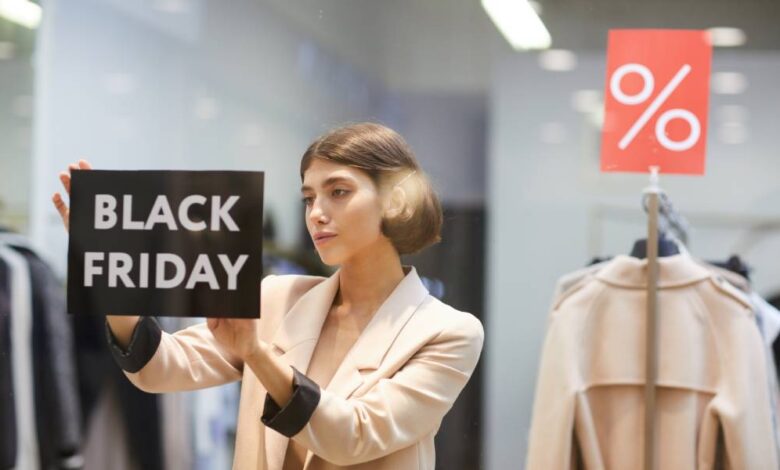 A woman in a suit sticking a black sign that reads "Black Friday" on it to the inside of a store's display window.