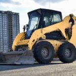 A skid steer sitting in a parking lot. There are some tall buildings in the background, and one of them is being worked on.