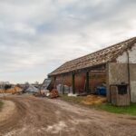 An older agricultural storage barn with new wooden rafters. Another barn restoration takes place across the path.