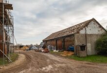 An older agricultural storage barn with new wooden rafters. Another barn restoration takes place across the path.