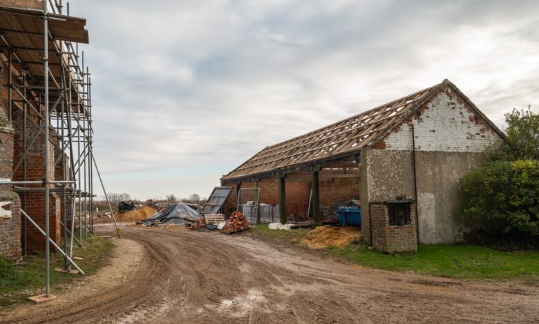 An older agricultural storage barn with new wooden rafters. Another barn restoration takes place across the path.