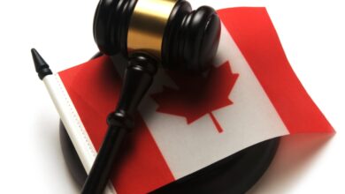 Close-up of a brown and gold gavel sitting on top of a small Canadian flag. The gavel is on a white table.