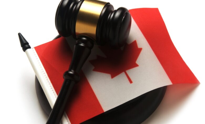 Close-up of a brown and gold gavel sitting on top of a small Canadian flag. The gavel is on a white table.