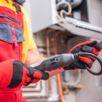 A person wearing red overalls and a yellow shirt is using a black and gray device. The background is blurry.