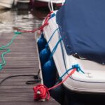 A modern motorboat with a blue canvas rain cover over the windshield and bow deck, docked at a weathered wood dock.