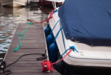 A modern motorboat with a blue canvas rain cover over the windshield and bow deck, docked at a weathered wood dock.