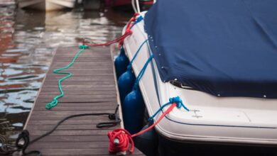 A modern motorboat with a blue canvas rain cover over the windshield and bow deck, docked at a weathered wood dock.