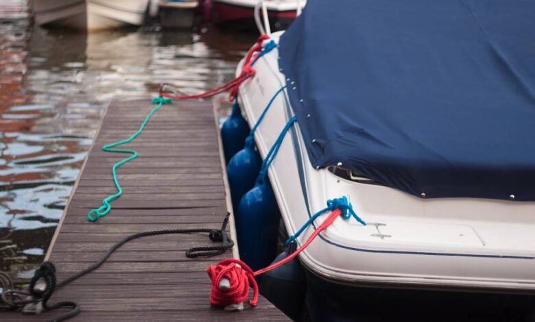 A modern motorboat with a blue canvas rain cover over the windshield and bow deck, docked at a weathered wood dock.