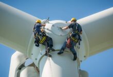 Two people hanging on the side of a wind turbine. They're both wearing harnessing gear and helmets.