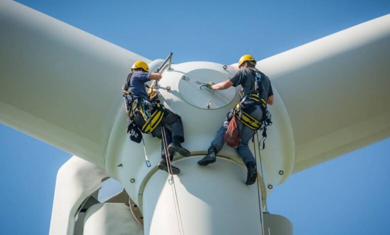 Two people hanging on the side of a wind turbine. They're both wearing harnessing gear and helmets.