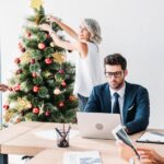 A group of four professionals in an office room. Two are working at a desk while two decorate a Christmas tree.