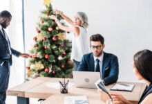 A group of four professionals in an office room. Two are working at a desk while two decorate a Christmas tree.