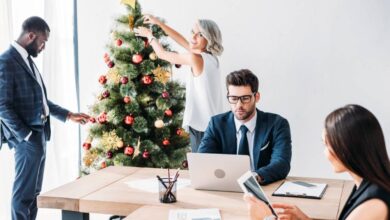 A group of four professionals in an office room. Two are working at a desk while two decorate a Christmas tree.