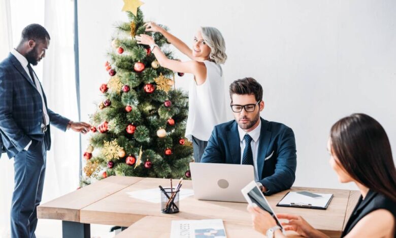 A group of four professionals in an office room. Two are working at a desk while two decorate a Christmas tree.