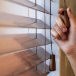 A homeowner holding onto their window treatment pulley cord. They are adjusting the settings on the window blinds.