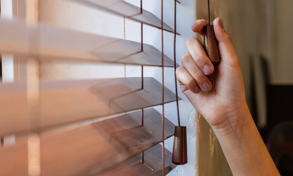 A homeowner holding onto their window treatment pulley cord. They are adjusting the settings on the window blinds.