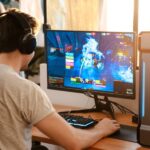 An online gamer sitting at his gaming desk with a headset on and an ergonomic chair. He's actively in-game.