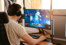 An online gamer sitting at his gaming desk with a headset on and an ergonomic chair. He's actively in-game.