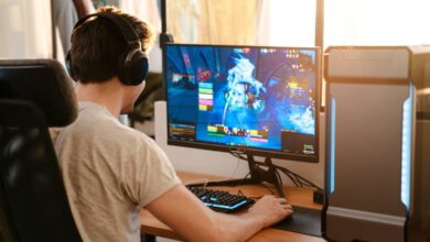 An online gamer sitting at his gaming desk with a headset on and an ergonomic chair. He's actively in-game.