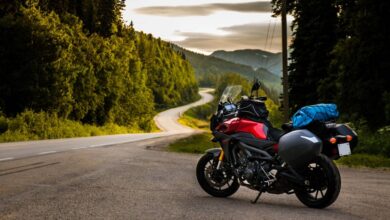 A motorcycle parked on the side of a curvy, twisty road. The sun is going down behind the tree line.