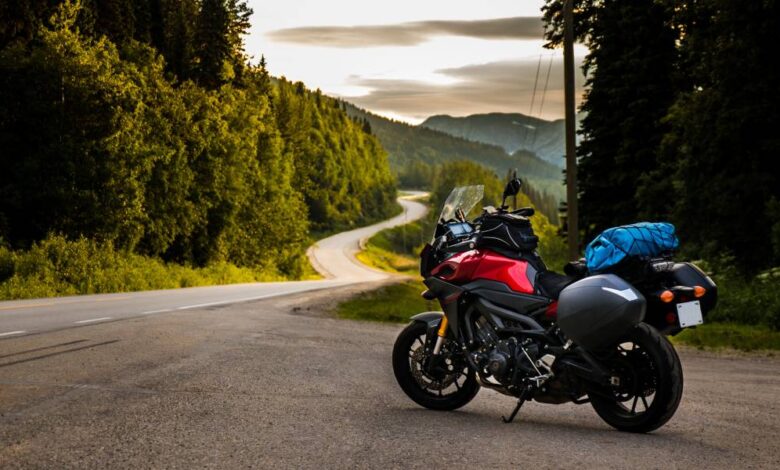 A motorcycle parked on the side of a curvy, twisty road. The sun is going down behind the tree line.