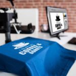 A blue t-shirt draped over a white table that says, "I run on coffee and donuts." The computer next to it says the same thing.