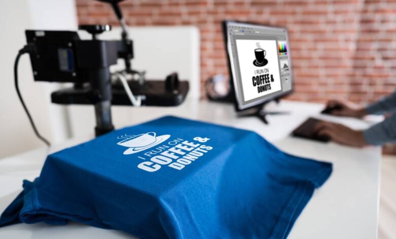 A blue t-shirt draped over a white table that says, "I run on coffee and donuts." The computer next to it says the same thing.