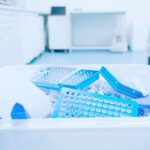 A disposal container in a laboratory is filled with latex gloves and waste. The room seems well-organized and clean.