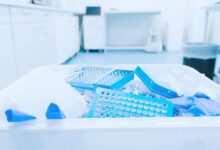 A disposal container in a laboratory is filled with latex gloves and waste. The room seems well-organized and clean.