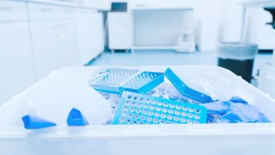 A disposal container in a laboratory is filled with latex gloves and waste. The room seems well-organized and clean.