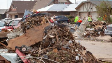 A pile of debris, including tree branches and demolished structures, in a neighborhood after a tornado has hit.