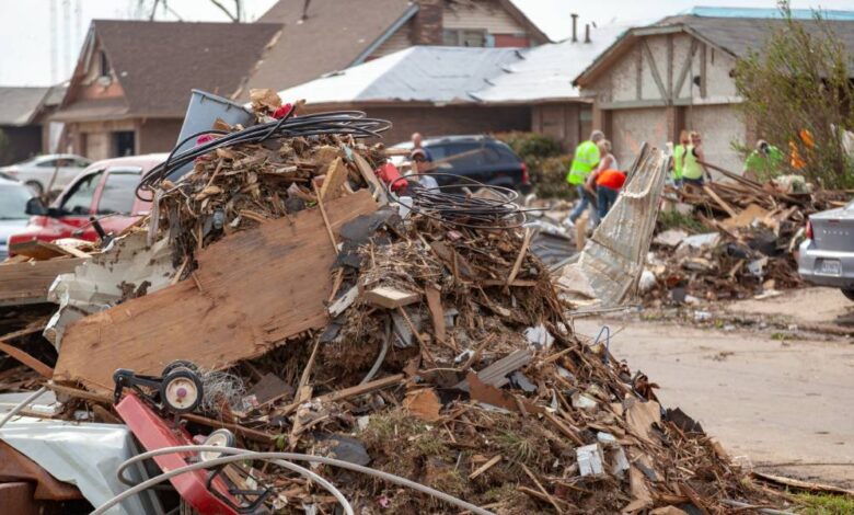 A pile of debris, including tree branches and demolished structures, in a neighborhood after a tornado has hit.