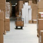 Large, brown cardboard boxes create a pathway through a warehouse. A gray cart sits in the pathway.