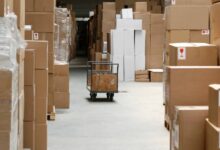 Large, brown cardboard boxes create a pathway through a warehouse. A gray cart sits in the pathway.