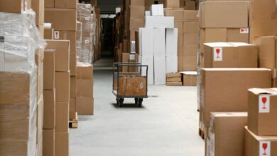 Large, brown cardboard boxes create a pathway through a warehouse. A gray cart sits in the pathway.