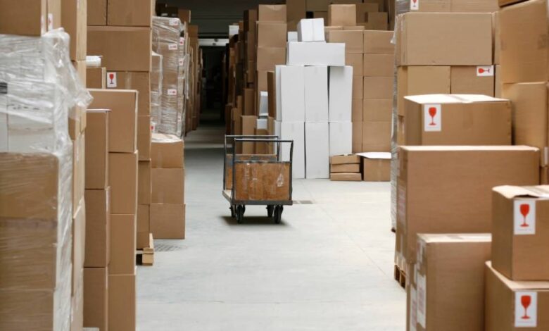 Large, brown cardboard boxes create a pathway through a warehouse. A gray cart sits in the pathway.