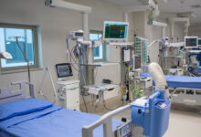 A row of hospital beds with small windows above them surrounded by different types of medical equipment.